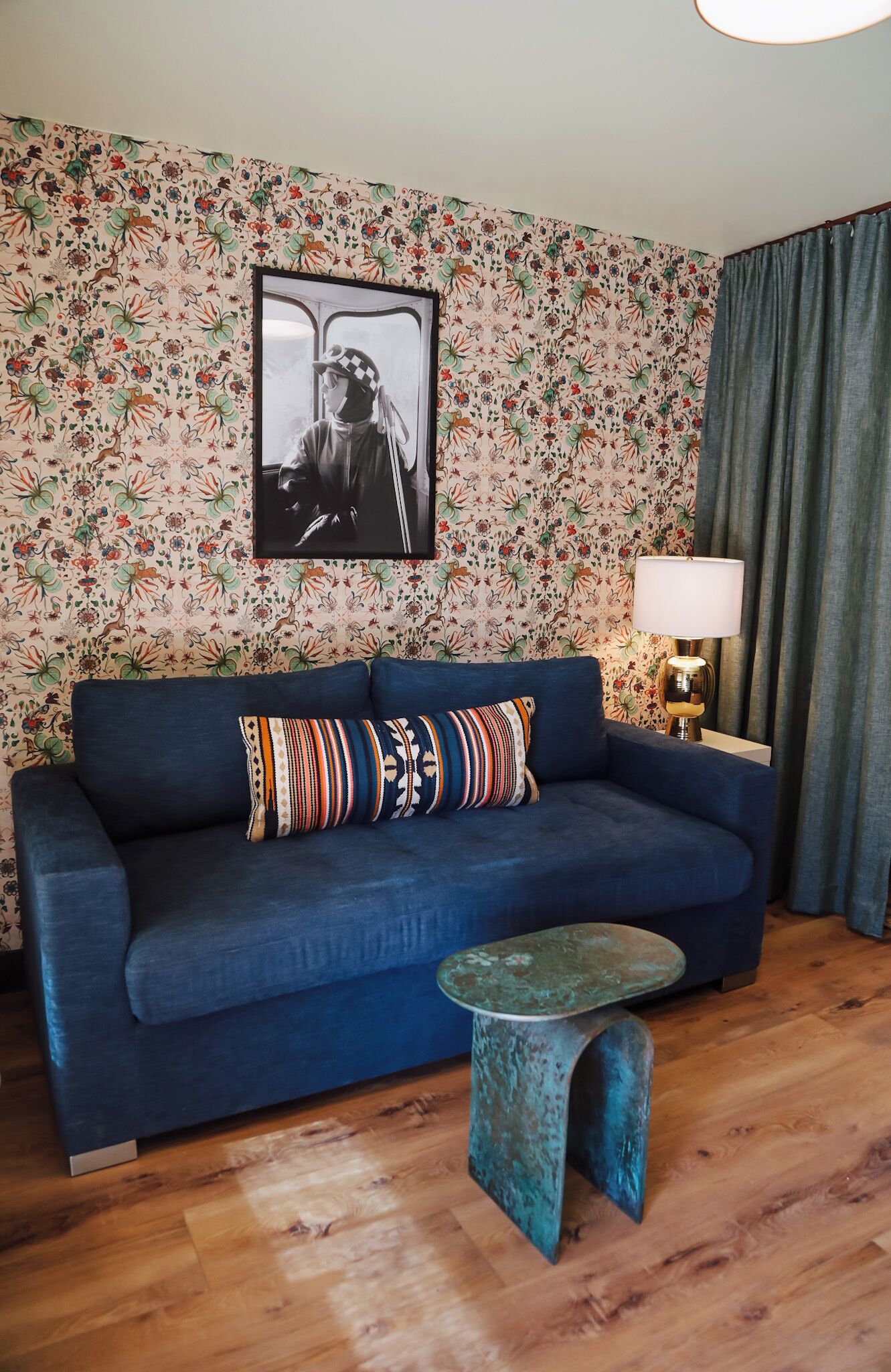 A living room with a blue sofa, patterned cushions, a framed picture, a lamp, and a small table.