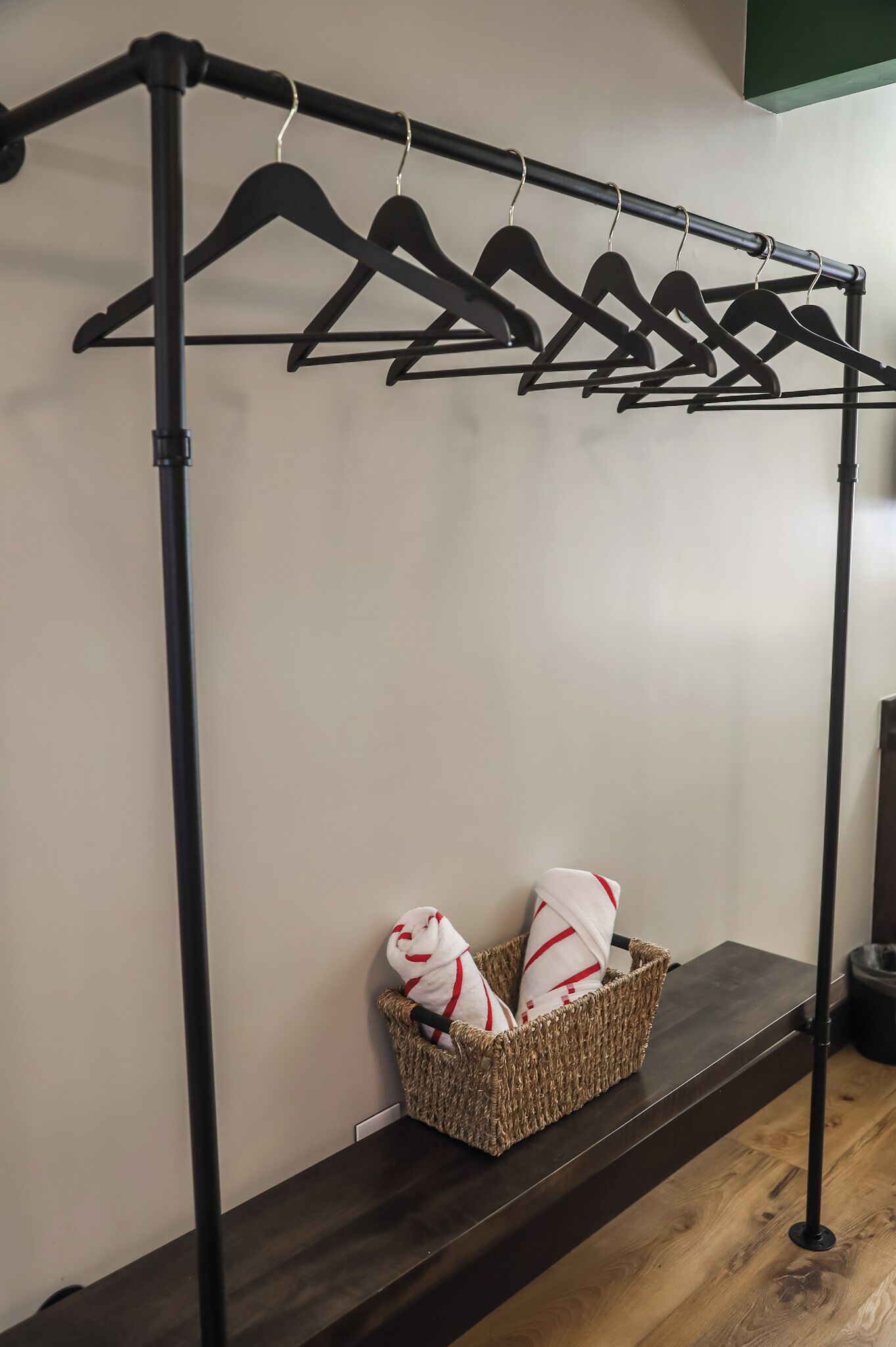 A clothing rack with multiple hangers, a woven basket with pillows, and a dark wooden shelf.