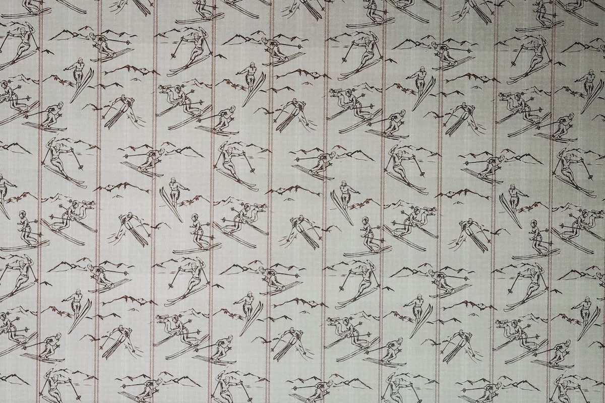 A bed with white linens and a metal headboard, set against a wallpaper with a ski pattern.