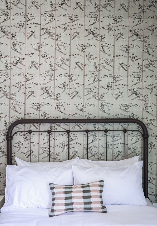 A bed with white linens and a metal headboard, set against a wallpaper with a ski pattern. - Altus Lodge (Silverton)
