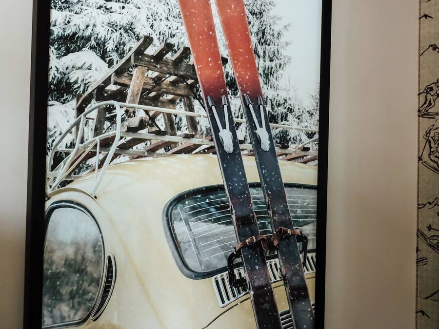 A framed picture of a vintage car with skis on the roof, set against a snowy landscape.