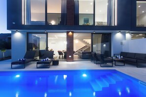 Una casa moderna con piscina, mobiliario de exterior y una escalera que lleva a un nivel superior.