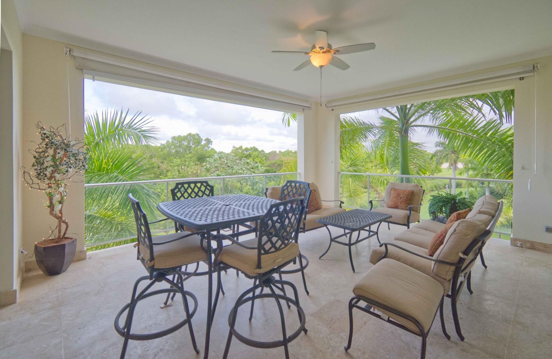 A covered patio with a table and chairs, a ceiling fan, and a view of the surrounding greenery.