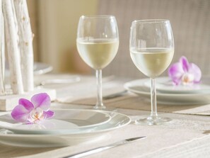A table set with white plates, two glasses of white wine, and purple orchid flowers. - Oostzee Swantje (Heiligenhafen)