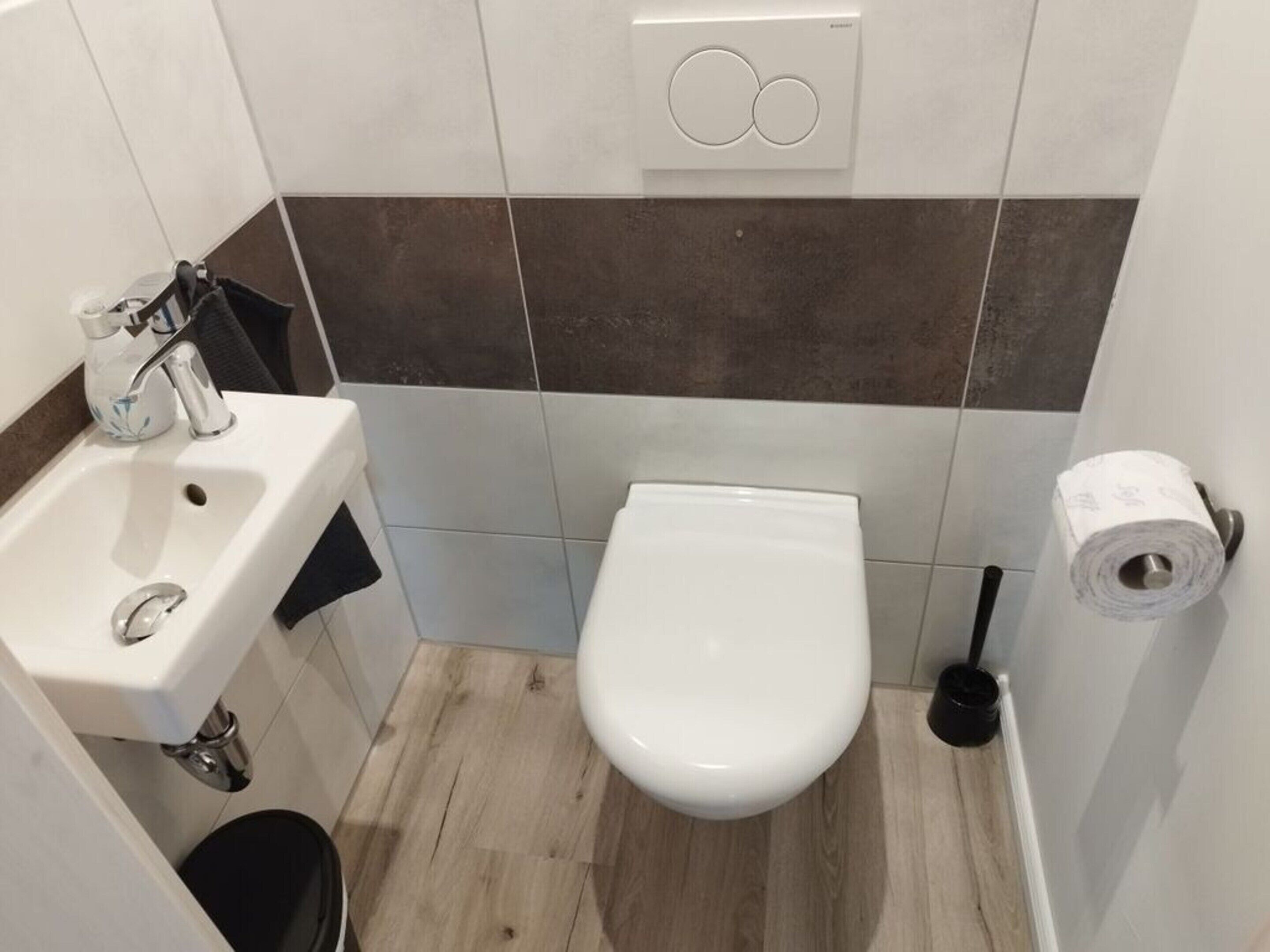 Et lille badeværelse med toilet, vask og toiletpapirholder.