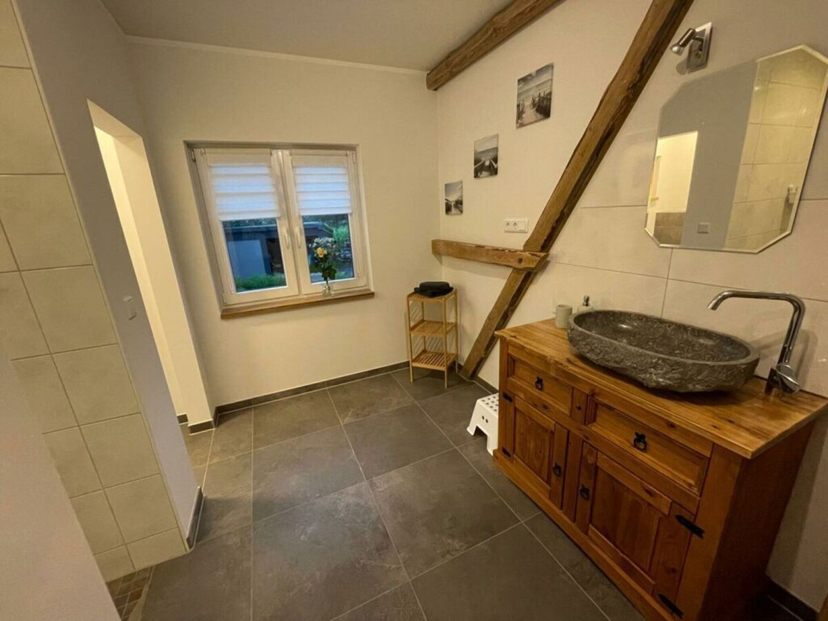 A bathroom with a stone sink, wooden vanity, a window with blinds, and a mirror on the wall.