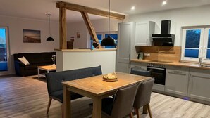 A modern kitchen with a wooden table and chairs, a built-in oven, and a window with a view. - Little Freedom Modern Retreat (Juebek)