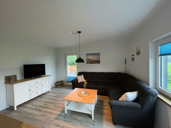 A living room with a TV, a sofa, a coffee table, and a window.