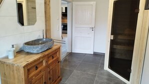 A bathroom with a stone sink, wooden cabinets, a mirror, and a door leading to another room. - Little Freedom Modern Retreat (Juebek)