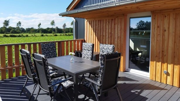 A wooden deck with a table and chairs, overlooking a green field. - Little Freedom Modern Retreat (Juebek)