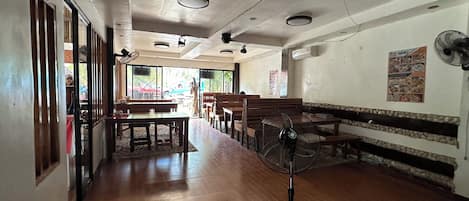A restaurant with wooden benches and tables, a fan, and a menu poster on the wall.