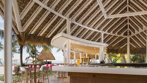 A beachside bar with wooden flooring, white pillars, and a thatched roof. - HDM 333 - Golf View Apartment in Exclusive Resort Access to Private Beaches (Punta Cana)