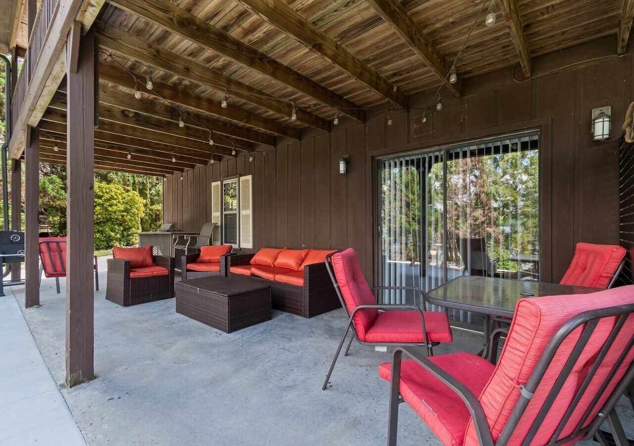 Un patio al aire libre con mobiliario de mimbre, una mesa de vidrio y una zona cubierta con vigas de madera.