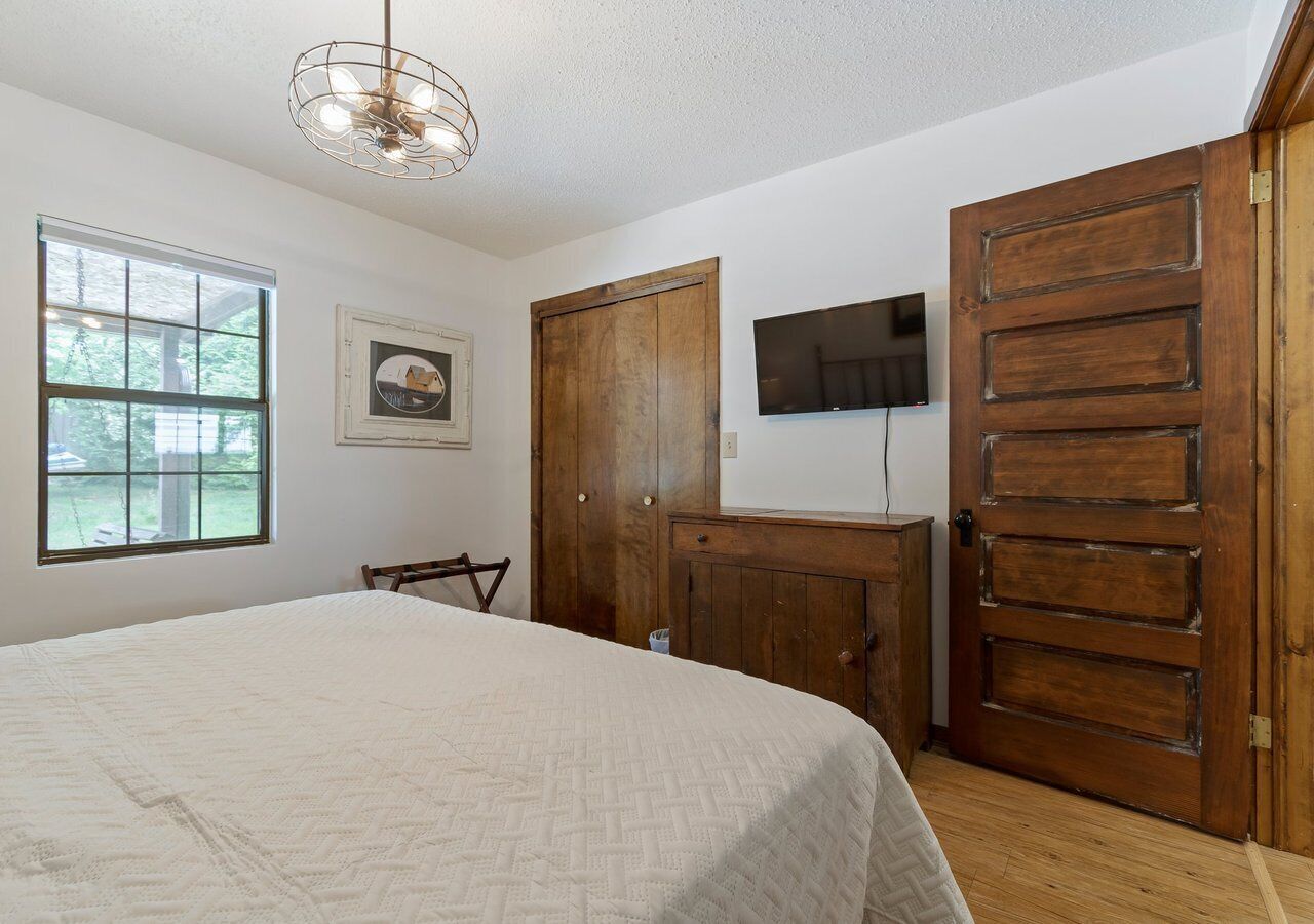 Une chambre à coucher avec un lit, une armoire en bois, un téléviseur fixé au mur et une fenêtre.