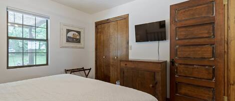 Une chambre à coucher avec un lit, une armoire en bois, un téléviseur fixé au mur et une fenêtre.