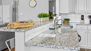 Una cocina moderna con armarios blancos, encimeras de granito, un lavamanos integrado y un reloj en la pared.