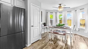 Una cocina moderna con un refrigerador de acero inoxidable, armarios blancos y un comedor con mesa y sillas de madera.