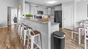 Una cocina moderna con armarios blancos, encimera de granito y una isla central con taburetes de bar.