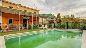 A swimming pool with a covered patio area, a stone archway entrance, and a fenced garden.