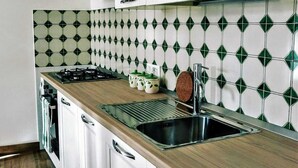 A kitchen with white cabinets, a wooden countertop, a stainless steel sink, and a patterned backsplash. - Comfy Apartment with lush Garden in the heart of  Sant Agata sui due Golfi (Massa Lubrense)