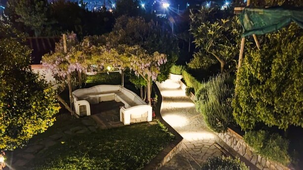 A well-lit garden area with a curved seating area and stone pathways. - Comfy Apartment with lush Garden in the heart of  Sant Agata sui due Golfi (Massa Lubrense)