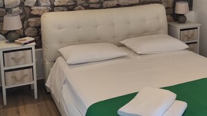 A bedroom with a stone wall, a tufted headboard, two bedside tables with lamps, and a green throw blanket. - Comfy Apartment with lush Garden in the heart of  Sant Agata sui due Golfi (Massa Lubrense)