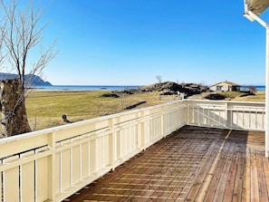 A wooden deck with a white railing overlooking a grassy landscape and a body of water. - 8 Person Holiday Home in Bremanger (Bremanger)
