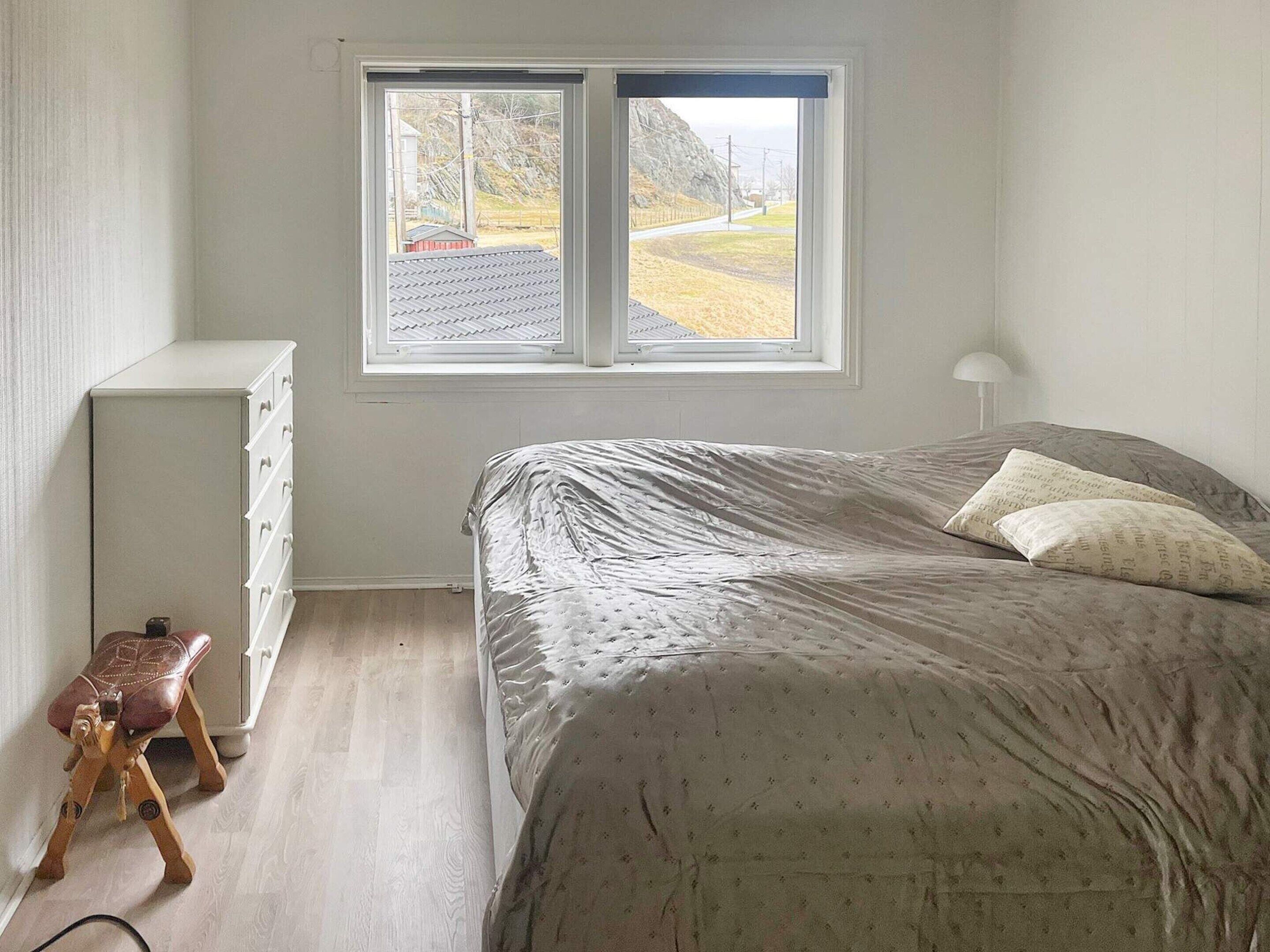 A bedroom with a bed, a dresser, a window, and a small stool.