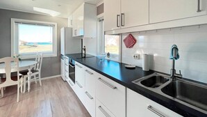 Eine moderne Küche mit weißen Schränken, einer schwarzen Arbeitsplatte und einem Edelstahlsp ülbecken. Ein Fenster bietet Blick auf den Strand.