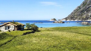 Ein Küstenanwesen mit einem kleinen Haus, grünen Feldern und freiem Blick auf das Meer und Felsen.