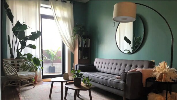 A living room with a grey sofa, a round mirror on the wall, a floor lamp, and several potted plants. - Private Deck Paradise  (Brooklyn)