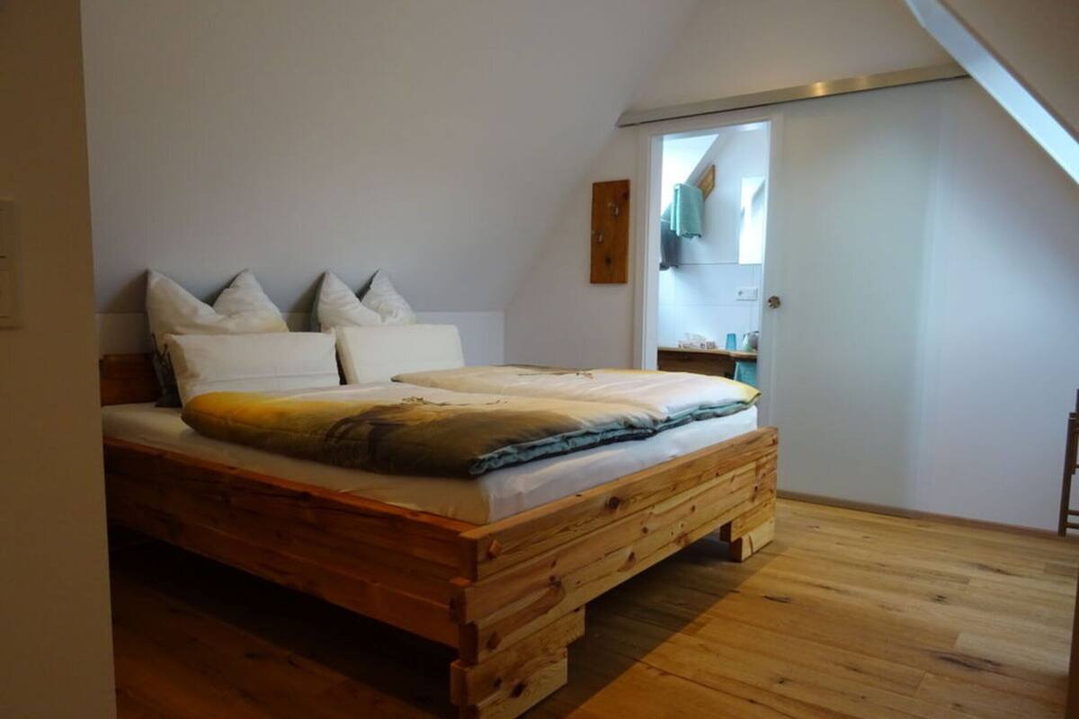 Quarto com cama de madeira, paredes brancas e teto inclinado.
