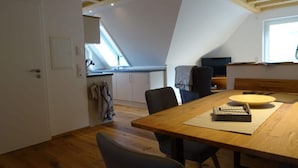 A dining area with a wooden table and chairs, a kitchen with a window, and a TV on a stand. - Holiday Apartment Kieschtock (Unterkirnach)