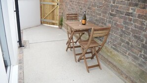 Eine Terrasse mit Holztisch und Stühlen, einer Weinflasche und einer Backsteinmauer.
