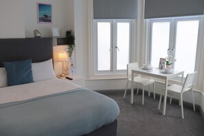 A bedroom with a bed, bedside table, lamp, and a window with a view.