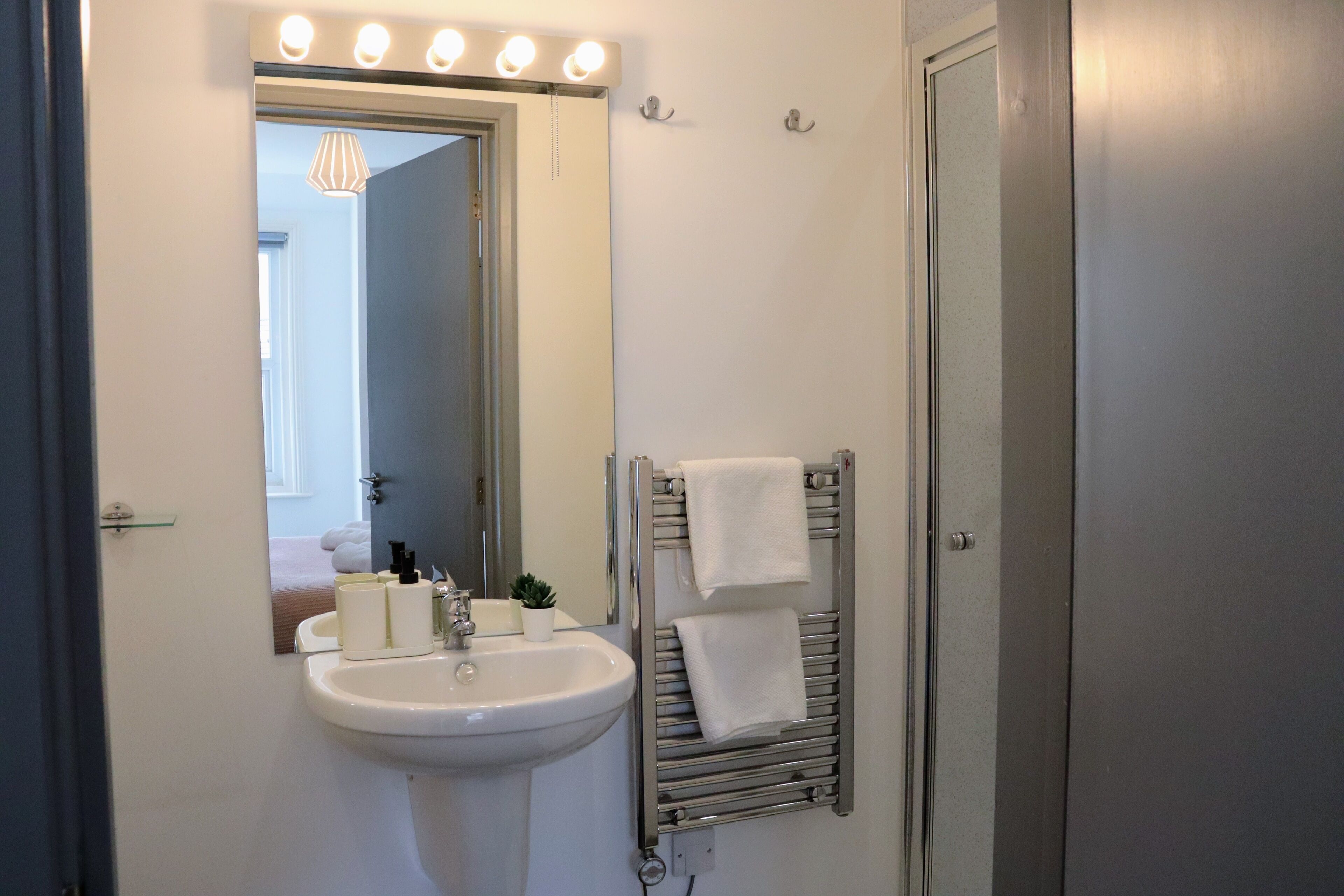A bathroom with a sink, mirror, towel rack, and a door.