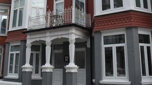 Ein mehrgeschossiges Wohnhaus mit Erker im Erdgeschoss, einem Balkon mit weißer Brüstung und einer roten Backsteinfassade.