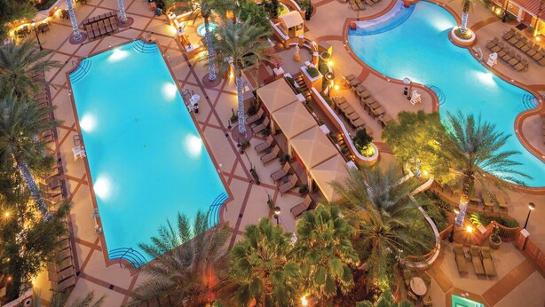 A hotel with two swimming pools, outdoor seating areas, and palm trees. - Wyndham Grand Desert 2 BR Deluxe - Full Resort Access -25% Deposit to Book NOW! (Las Vegas)