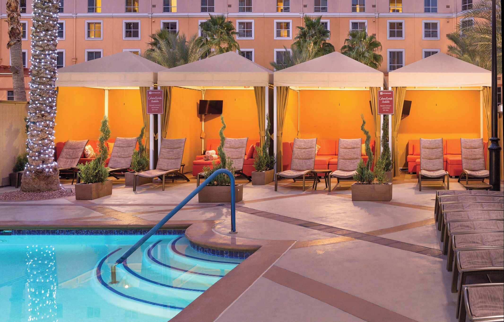 Un espace aménagé au bord de la piscine, avec des chaises longues et des parasols, une piscine dont le bord est bleu, et un bâtiment en arrière-plan.