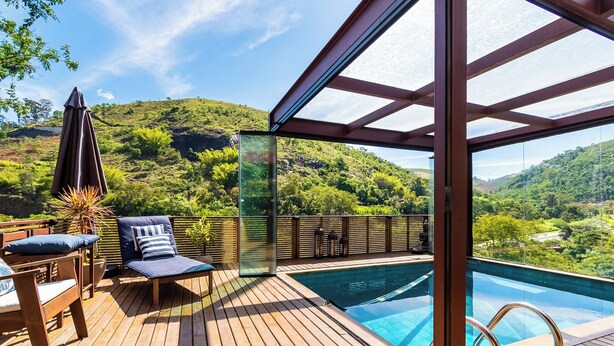 A wooden deck with a pool, lounge chairs, and a glass enclosure offering a view of a lush hillside. - Santa Serra Itaipava (Petrópolis)
