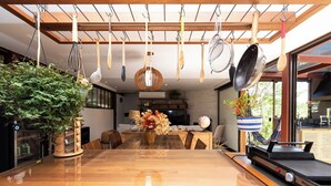 A modern kitchen with wooden cabinets, a large dining table, and hanging utensils. - Santa Serra Itaipava (Petrópolis)