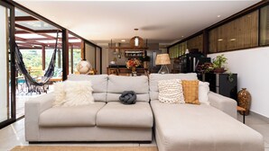 A modern living room with a large sectional sofa, a hammock, and a kitchen area in the background. - Santa Serra Itaipava (Petrópolis)