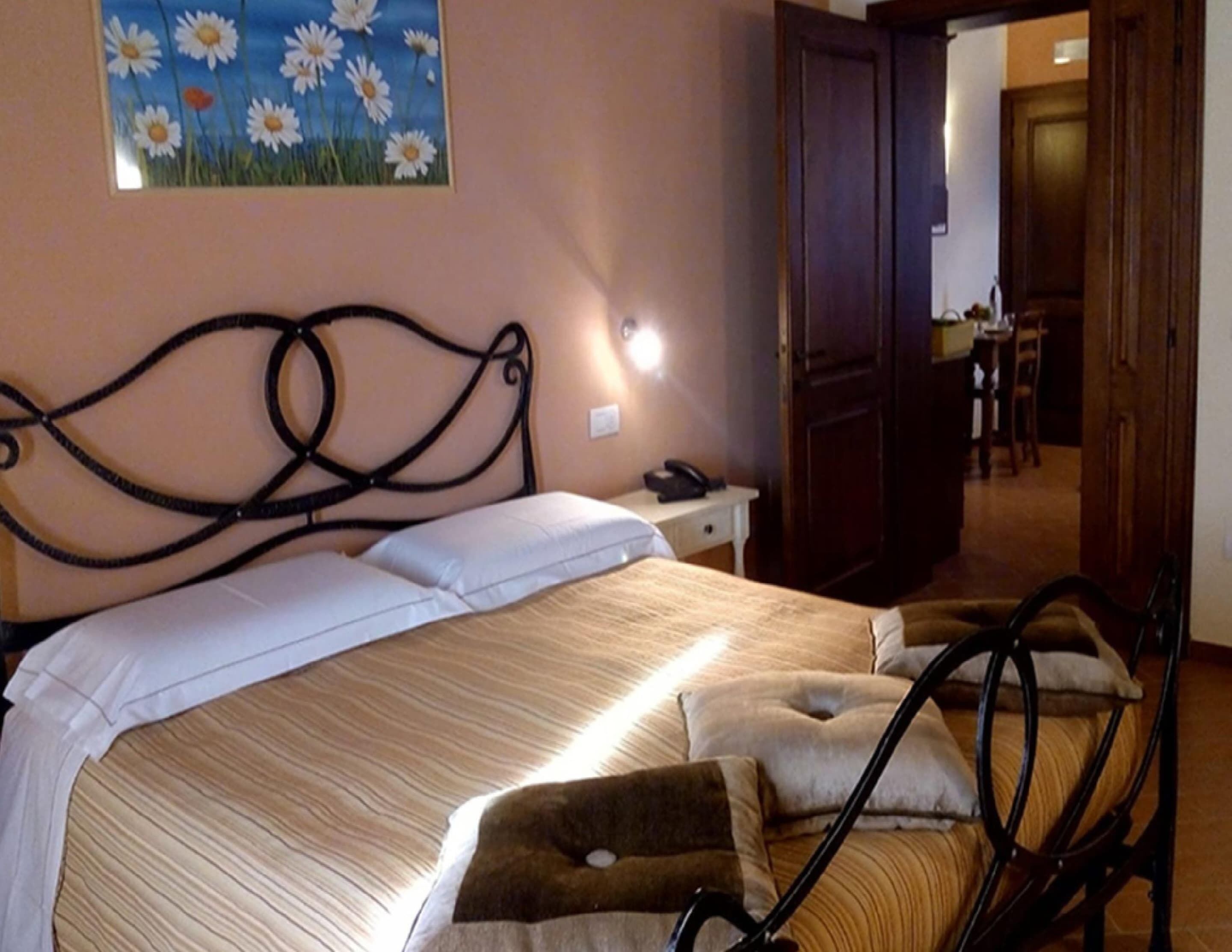 A neatly made bed with a striped bedspread and pillows, a wall-mounted light, and a painting of daisies.