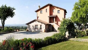 A two-story house with a stone facade, a small porch, and a well-maintained lawn with red flowers. - Casa Vacanze a Bettona con Giardino (Bettona)
