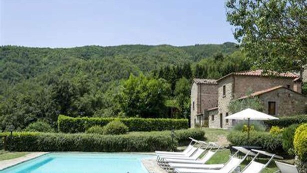 A swimming pool with lounge chairs, a stone building, and a forested hillside in the background. - Casa Vacanze a Bettona con Giardino (Bettona)