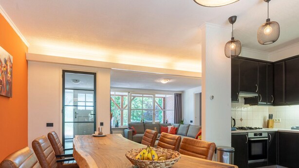 Une cuisine moderne avec des meubles de couleur sombre, un grand îlot central doté de sièges et des luminaires suspendus.