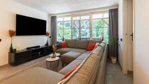 Un salon moderne doté d’une grande fenêtre, d’un téléviseur à écran plat et d’un ensemble de canapés.