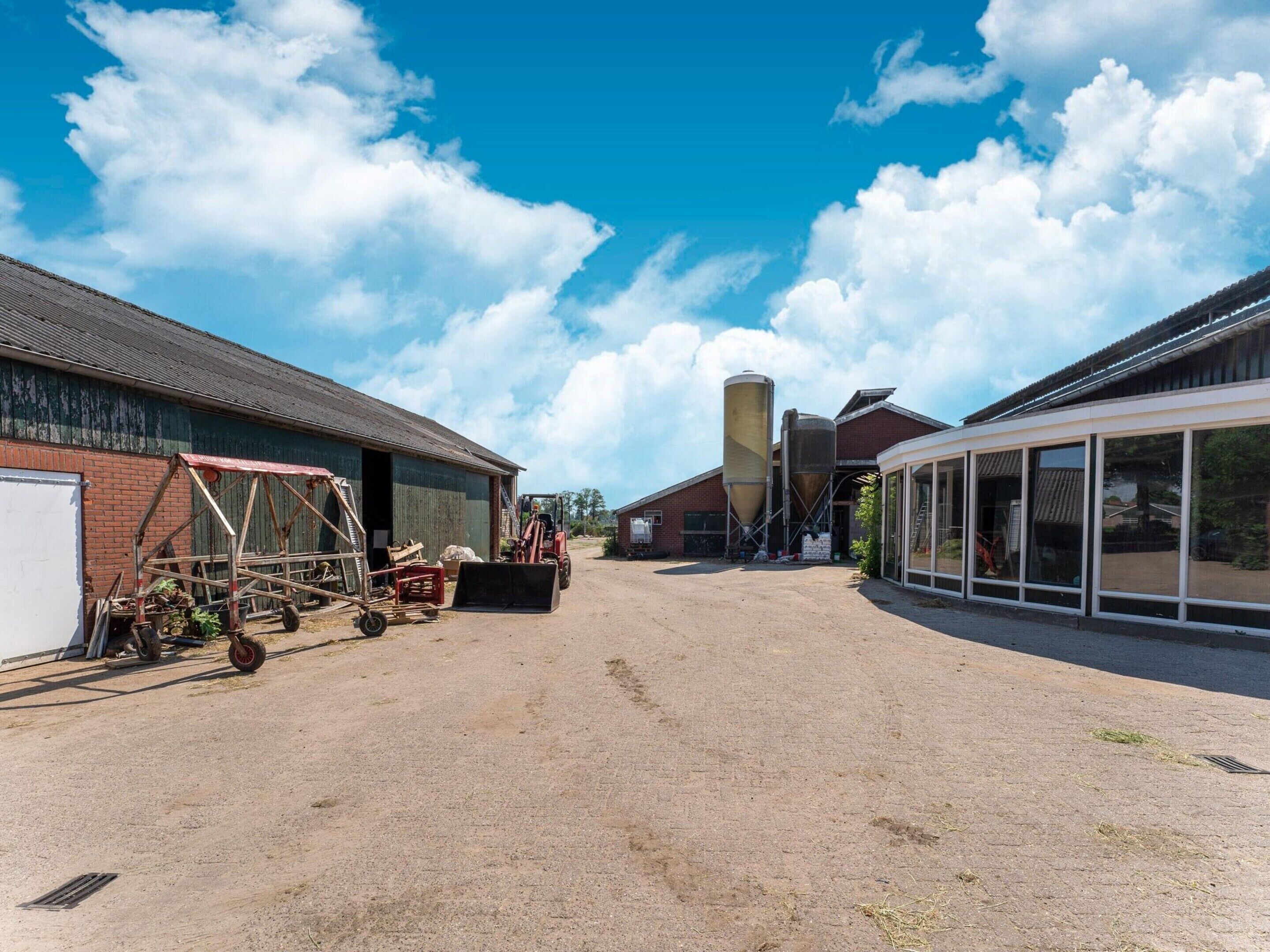 A spacious industrial area with a dirt ground, a large building with a metal roof, and a silo structure.