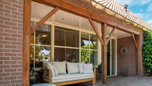 Une terrasse couverte avec un banc en bois et une petite table, de grandes fenêtres et un mur en briques.