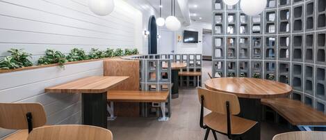 Un interno ristorante moderno con tavoli e sedie in legno, un'area con una panca curva e un parete con motivo a griglia.